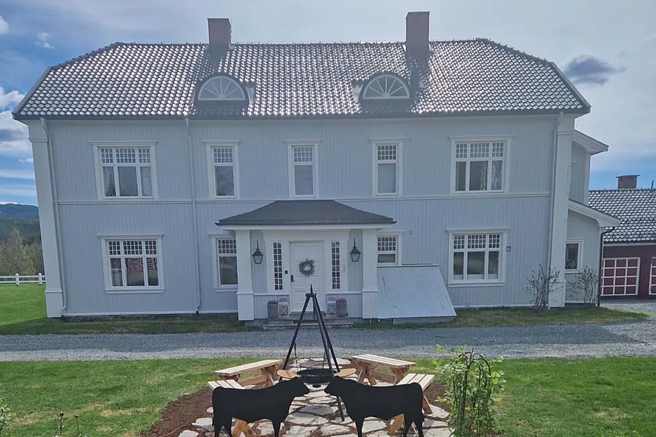 Hovedhuset sett rett forfra fra tunet, med bålpanna og Angus-silhuettene på plassen foran